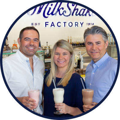 Three individuals posing together at a milkshake franchise, highlighting the team or customer experience. 