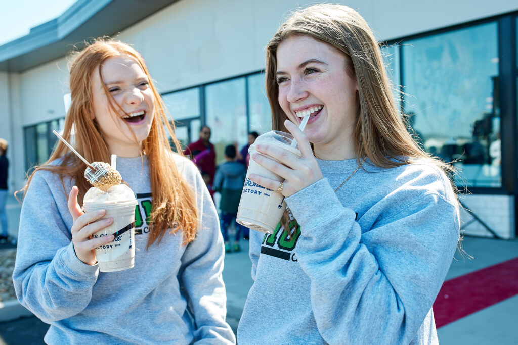 Two friends enjoying gourmet milkshakes at a dessert franchise, smiling and having a great time.