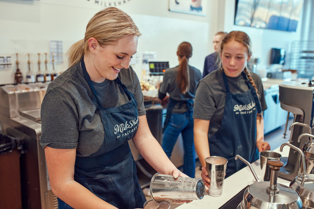 Team members preparing milkshakes behind the counter at a MilkShake Factory location.