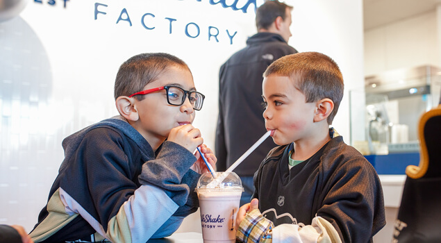 Two young boys enjoying milkshakes at a MilkShake Factory location.