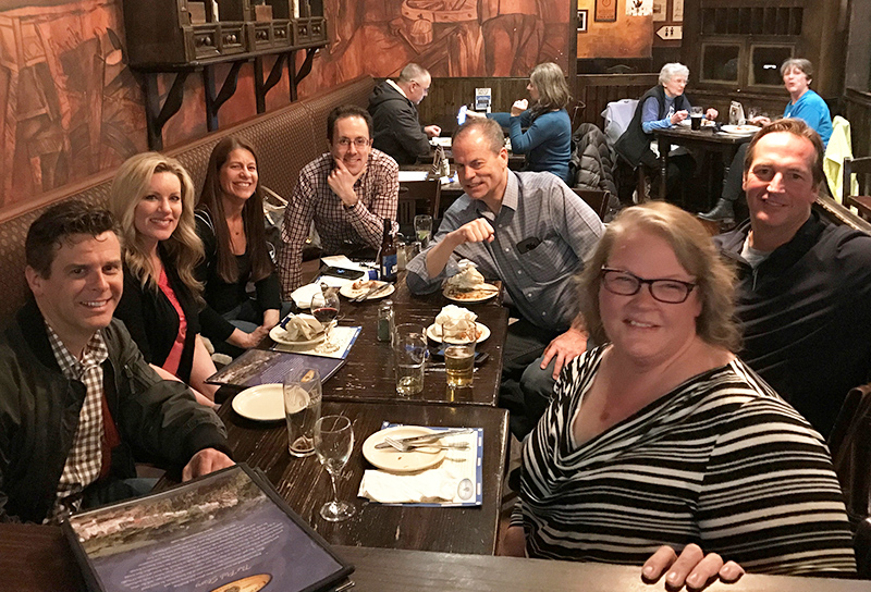 A group of people around a wooden table in a dim-lit restaurant smiling.