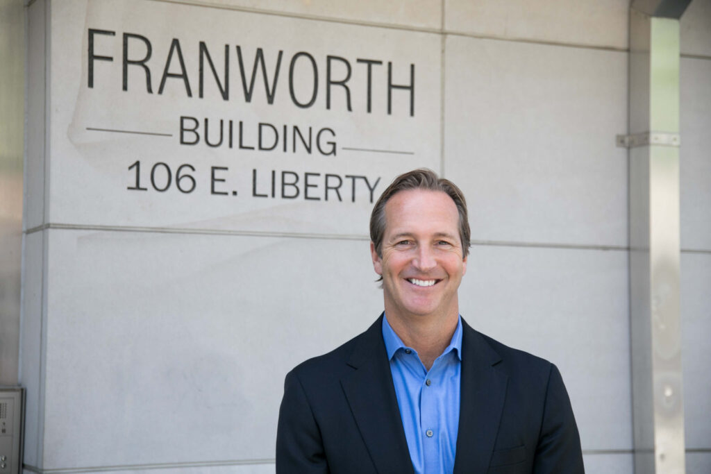 A man in a suit smiling in front of a building