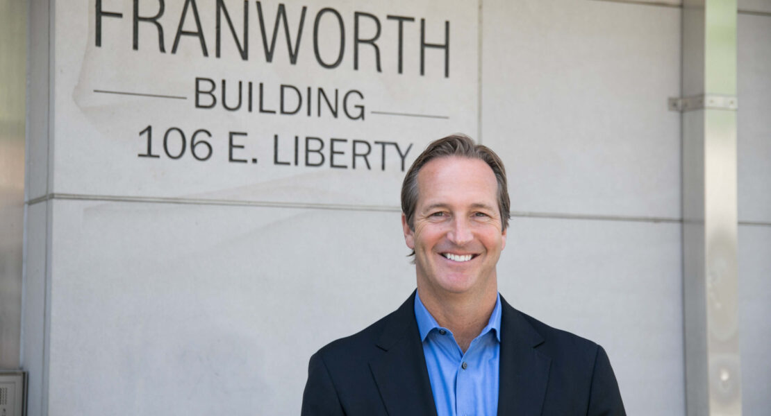 A man in a suit smiling in front of a building