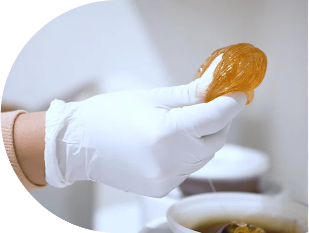 A sugarist holding a ball of sugar wax, ready for application during a sugaring hair removal session.