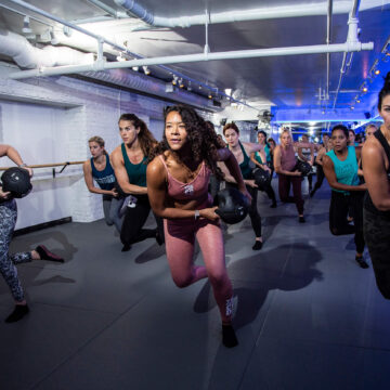 Women working out during a Barre Code class, in a dark room with a brick wall and a mirror wall. Scale your business with Franworth.