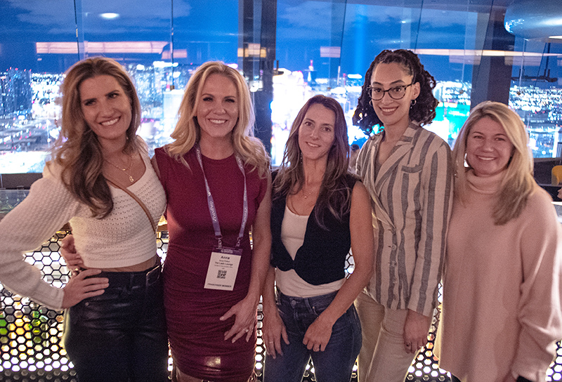 A group of female franchise professionals standing next to each other smiling, with glass walls behind them overlooking Las Vegas.