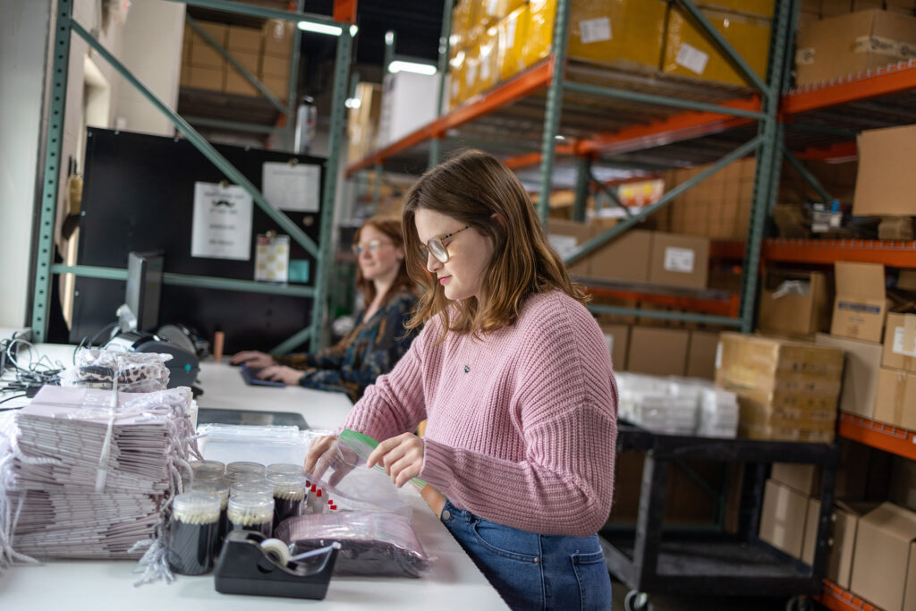 Liberty team member packaging Lash Lounge orders. There are many boxes behind her in the facility