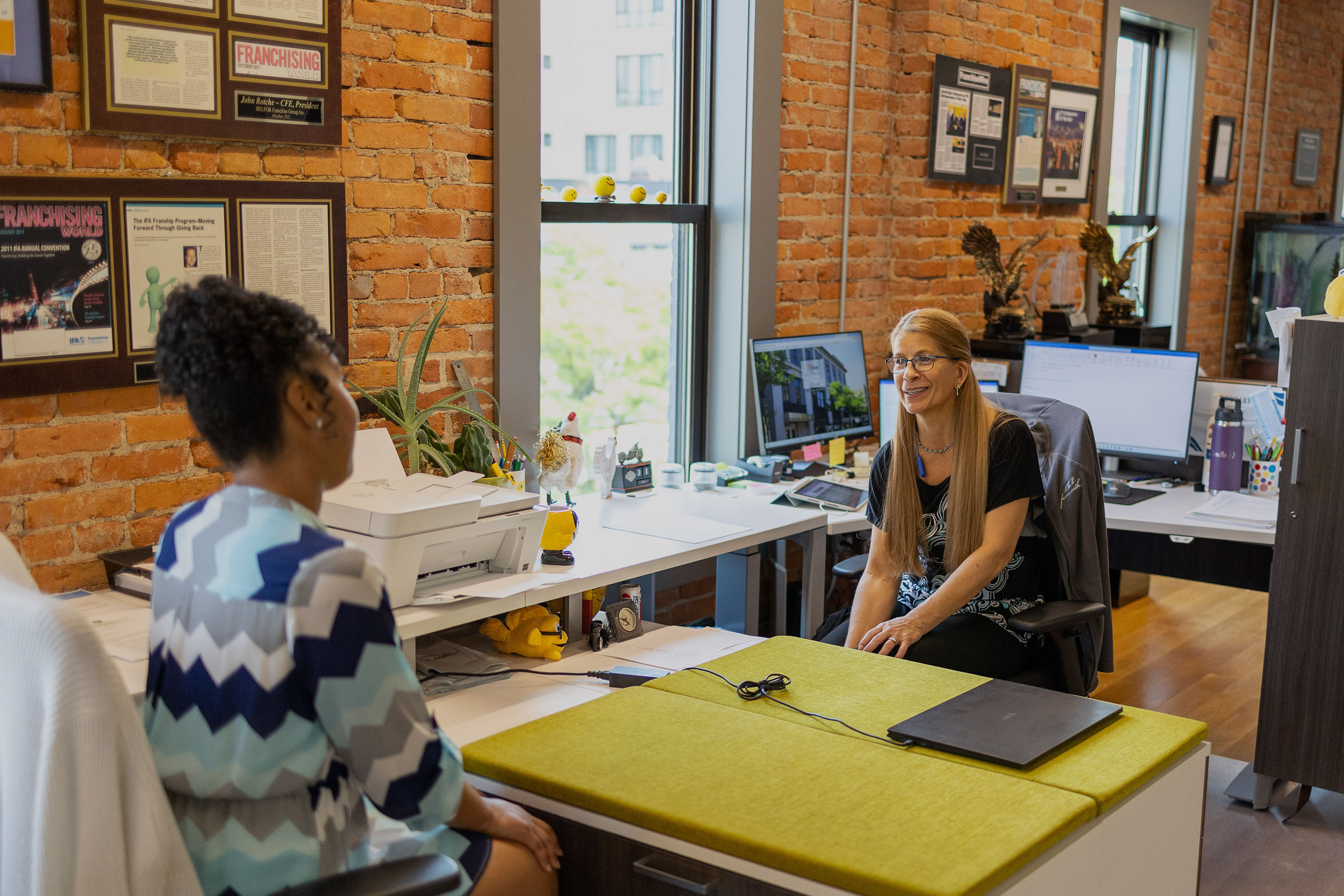 Two women sitting at desks in an office, discussing the advantages of franchising.