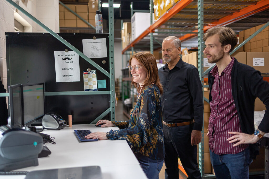 Liberty team members are looking at a computer screen, standing in front of many boxes behind them